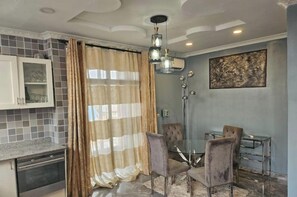 A modern kitchen with a dining area, featuring a glass table, chairs, and a pendant light.