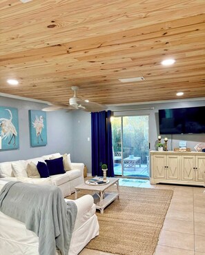 A modern living room with a wooden ceiling, a white sofa, a coffee table, and a TV. - The Laughing Seagull  Beach & Boats (Destin)