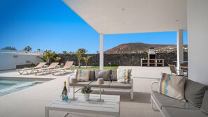A poolside area with lounge chairs, a sofa, and a table with a bottle and glass.