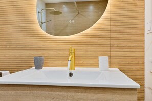 Een badkamer met een witte wastafel, een gouden kraan, een ronde spiegel en houten lambrisering.