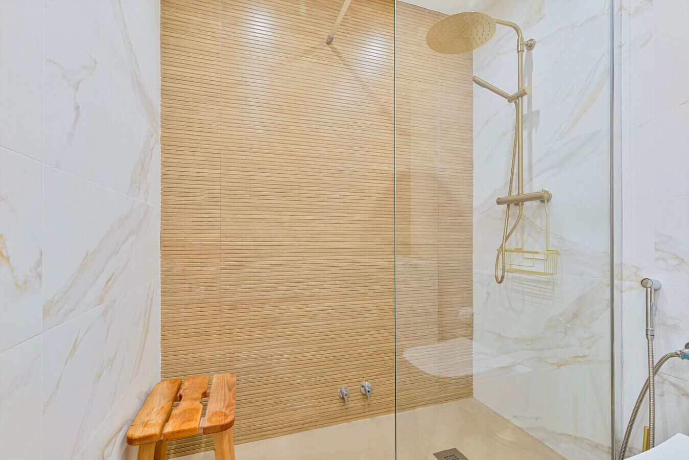 A modern shower with a glass enclosure, wooden panel wall, and a small wooden stool.