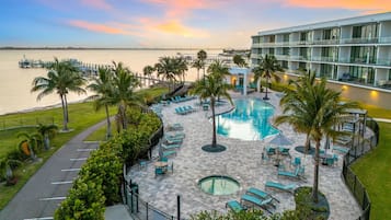 A resort pool area with lounge chairs, palm trees, and a view of the water.