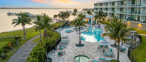 A resort pool area with lounge chairs, palm trees, and a view of the water.