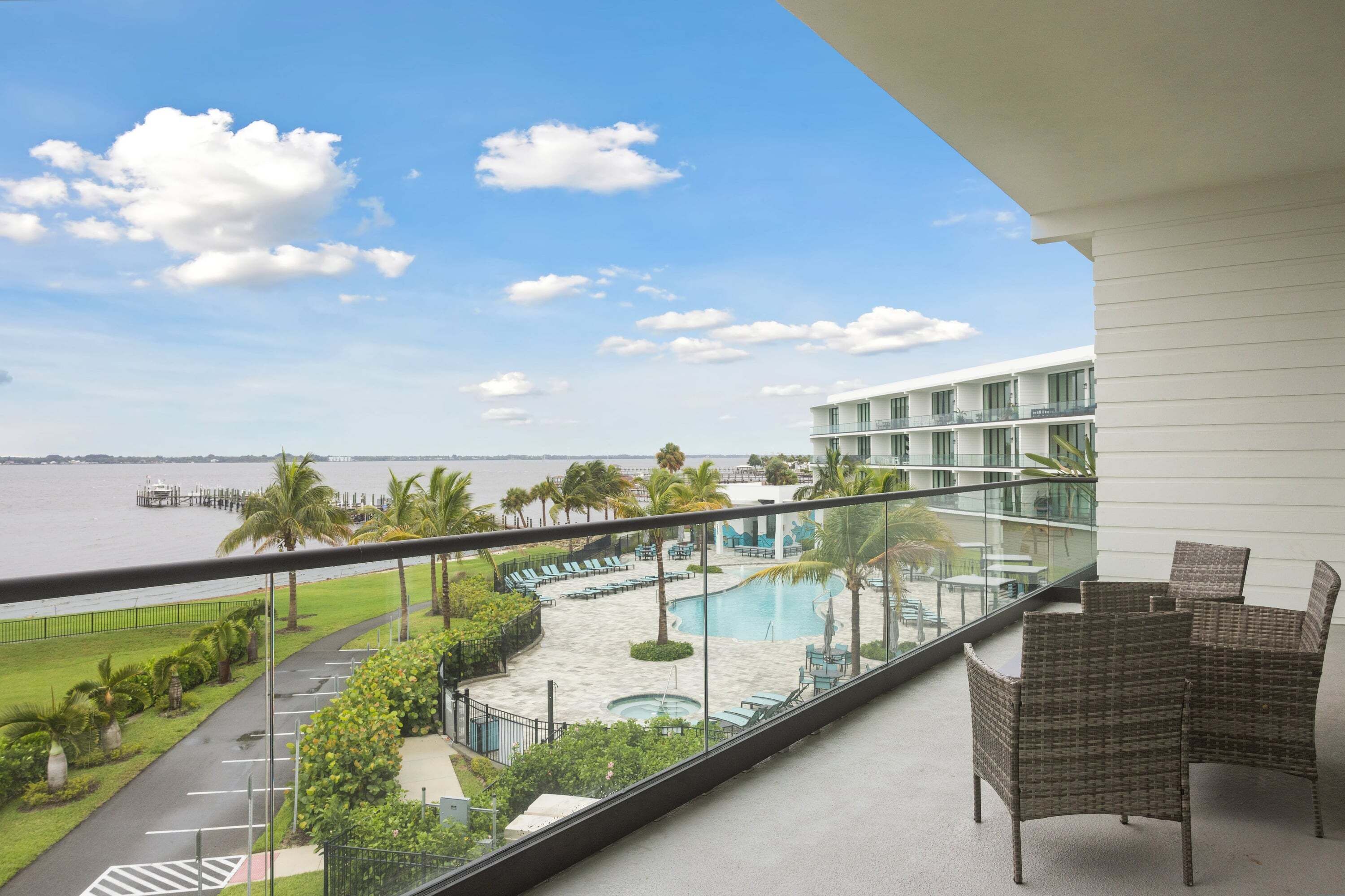 A balcony with wicker furniture overlooking a pool and a view of the water.