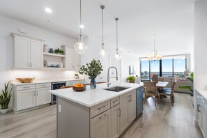 Une cuisine moderne dotée d’un grand îlot central, de luminaires suspendus et offrant une vue sur l’extérieur.