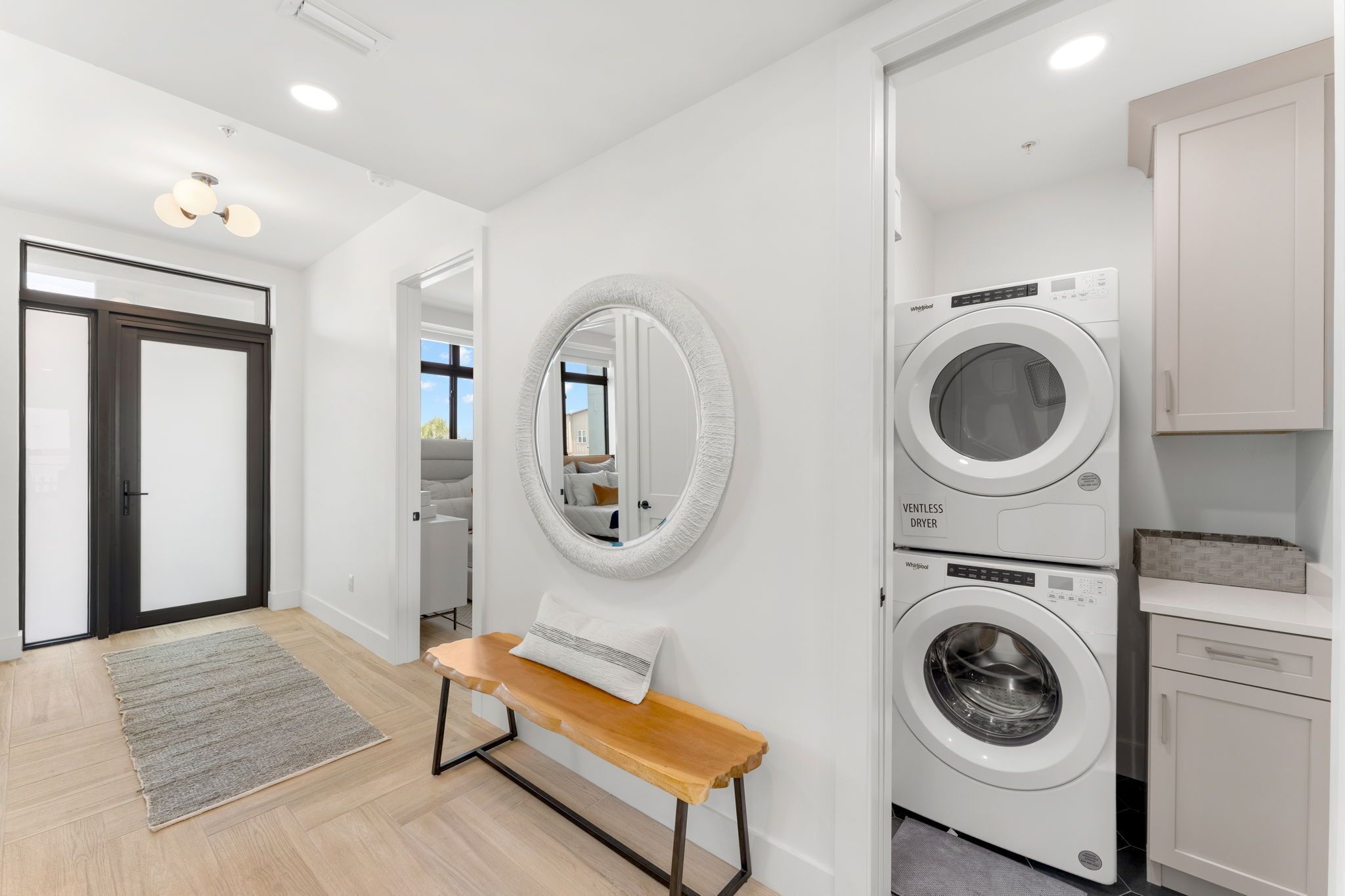 A laundry room with a bench, a round mirror, and two stacked washing machines.