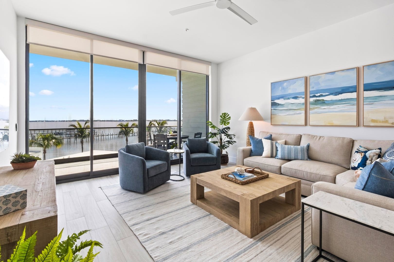 A modern living room with a large window overlooking a marina, a sofa set, a coffee table, and a ceiling fan.