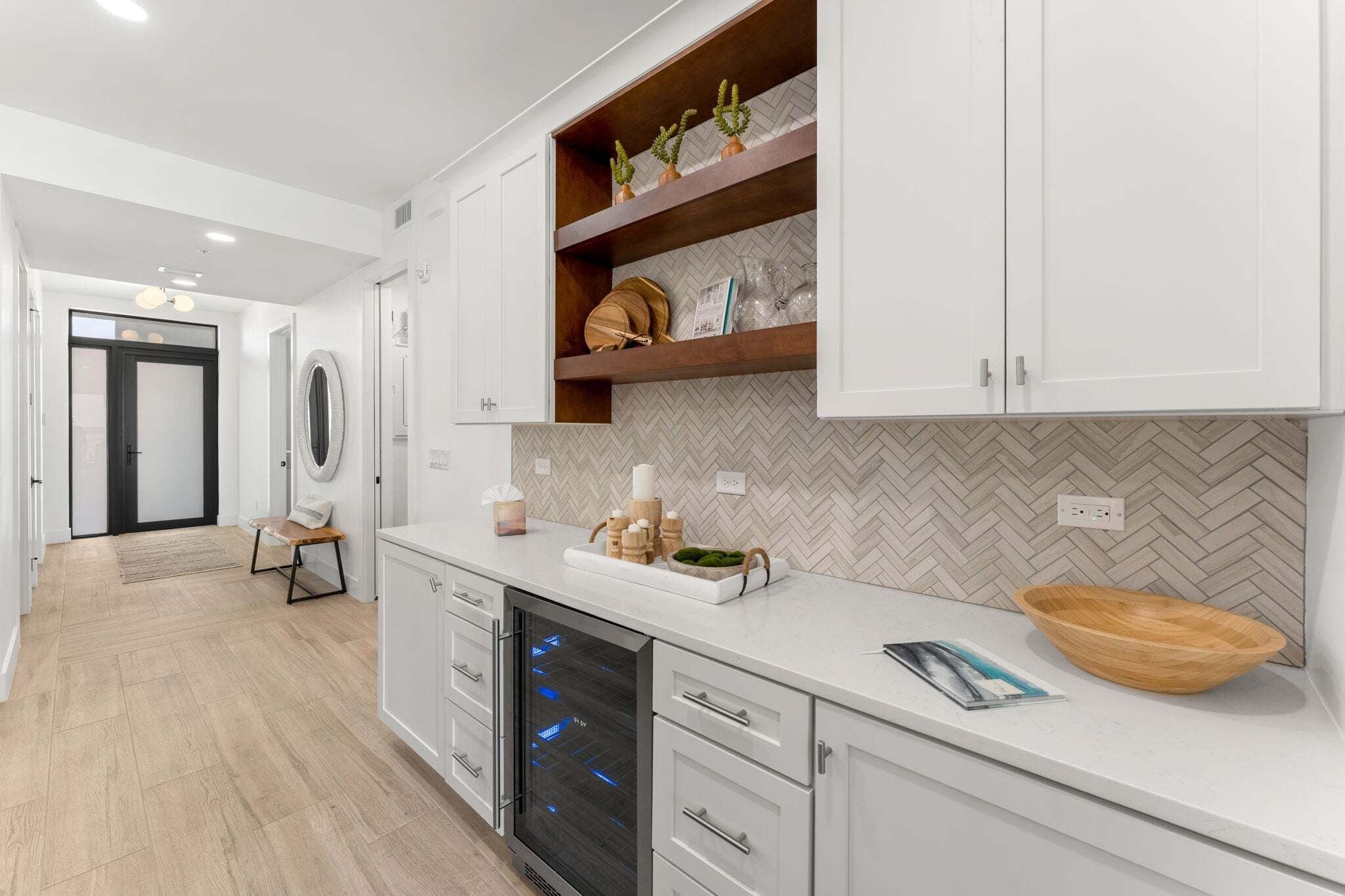 A modern kitchen with white cabinetry, a herringbone-patterned backsplash, and a wooden bowl on the counter.