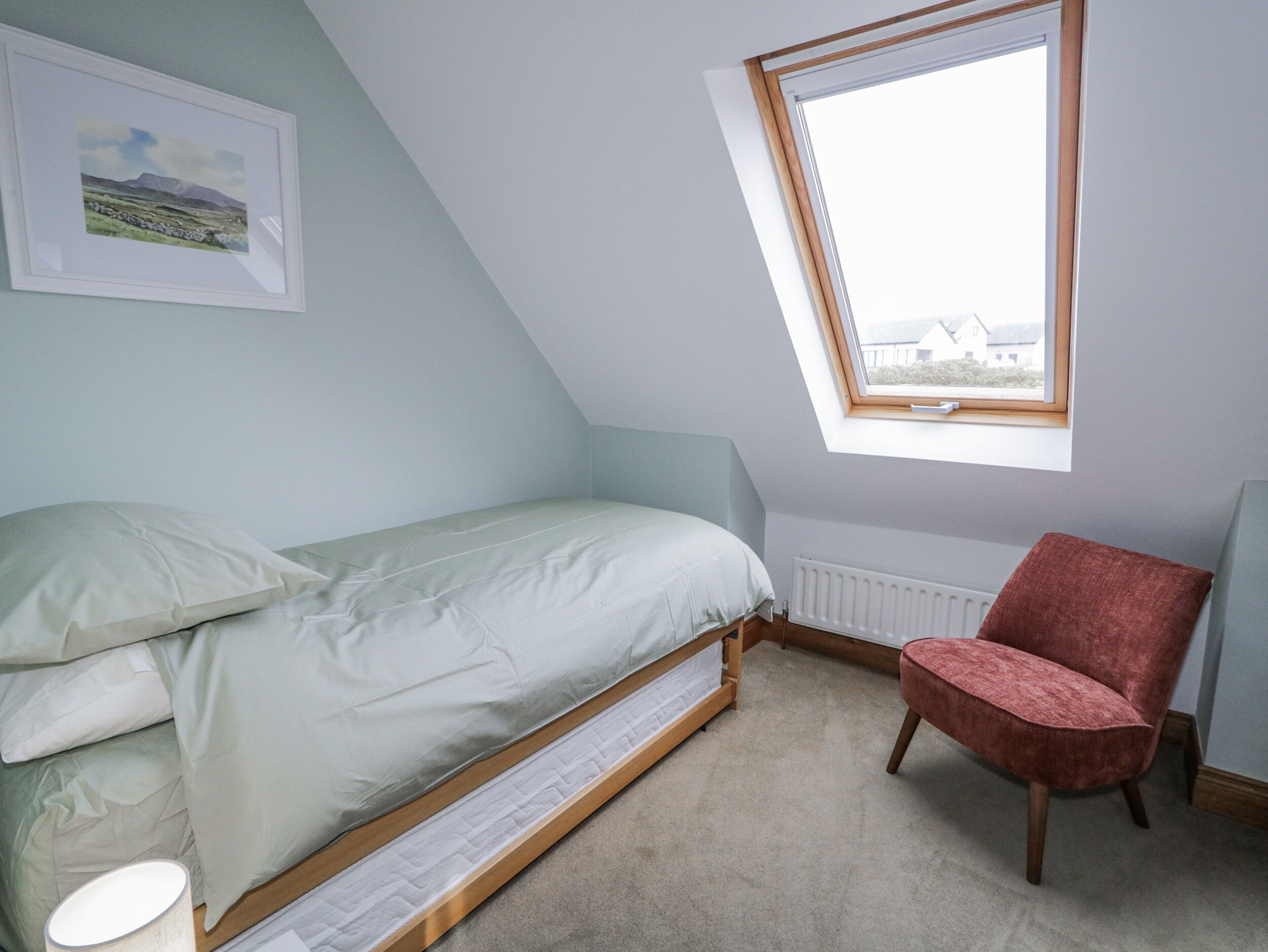 A bedroom with a bed, a red chair, a radiator, and a skylight.