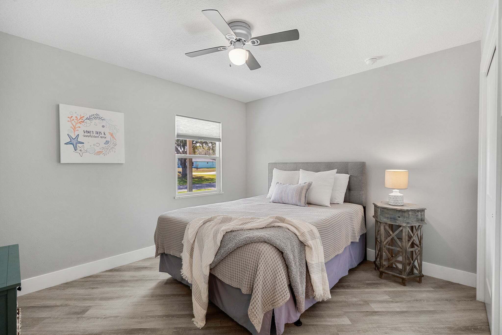 A bedroom with a bed, a ceiling fan, a window, and a bedside table with a lamp.