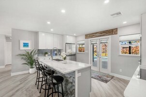 Una cocina moderna con una isla de mármol, taburetes de bar y una planta en maceta.