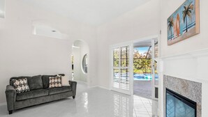 A spacious living room with a grey sofa, a fireplace, and a view of a pool through a glass door. - 218 Cherry Drive (Melbourne Beach)
