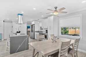 A modern kitchen with white cabinetry, a marble island, and a dining area with wooden chairs. - 1544 Lime Drive (Melbourne)