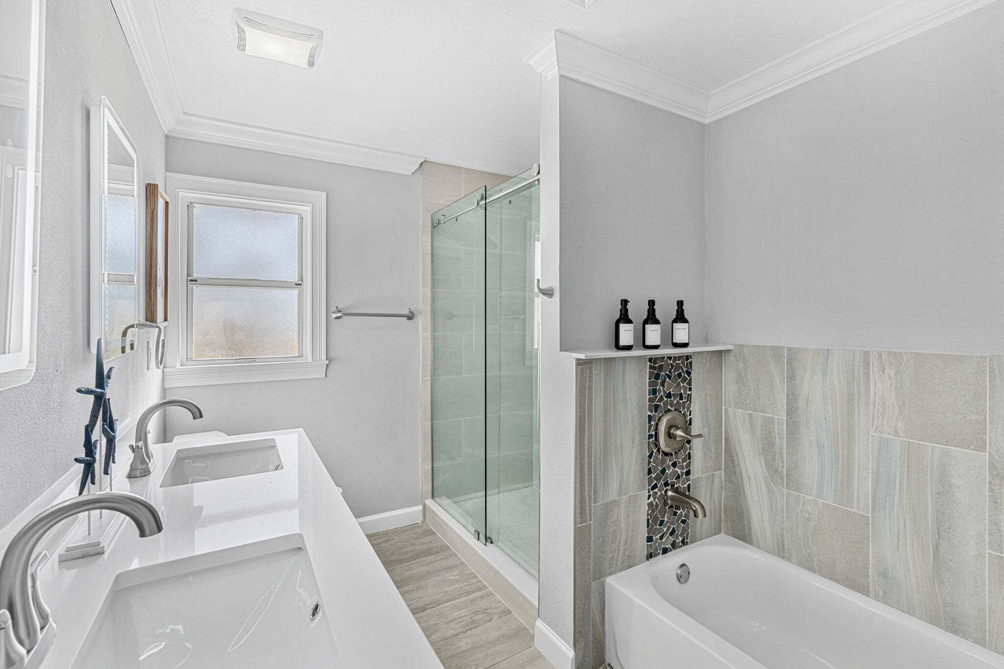 A modern bathroom with a glass shower enclosure, a large bathtub, and a vanity with two sinks.