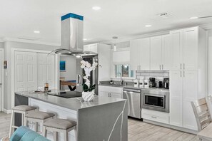 A modern kitchen with white cabinetry, a stainless steel range hood, a built-in microwave, and a central island with bar stools. - 1544 Lime Drive (Melbourne)