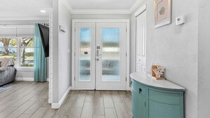 Un couloir avec une double porte, un mur de couleur claire, un meuble turquoise et une fenêtre avec des rideaux.