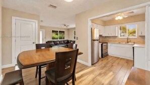 A spacious kitchen with a dining area, wooden flooring, and a ceiling fan. - Lux 3BD House, 5 Min To Holly Cross, HCA Hospital&Beaches (Oakland Park)