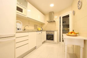 A kitchen with white cabinets, a dishwasher, an oven, and a fruit bowl on the counter. - Apartment Veleta (Port de Pollença)