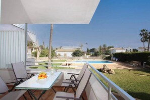 A balcony with a table and chairs, overlooking a swimming pool and a garden. - Apartment Veleta (Port de Pollença)