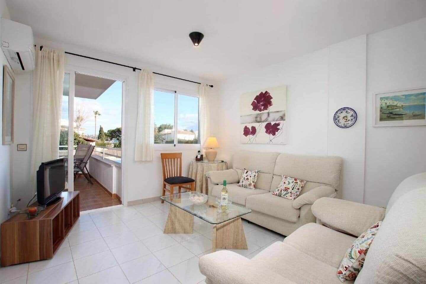 Un soggiorno con divano, tavolino in vetro, televisione e una poltrona. È presente un balcone con vista mare.