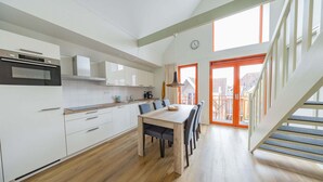 Een moderne keuken met witte kasten, een houten eettafel en een trap naar een buitenruimte.