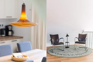 Une cuisine moderne avec un luminaire suspendu orange, une table à manger surmontée d’un panier en osier et une chaise bleue.
