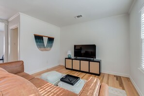 A living room with a sofa, ottoman, TV, and a woven cabinet.