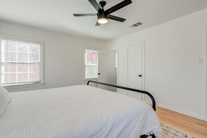 A bedroom with a bed, a ceiling fan, a window with blinds, and a door.