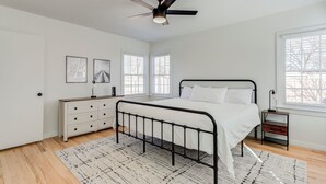 Un dormitorio con cama, ventilador de techo, ventana y mesita de noche.