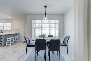 A dining area with a marble floor, a round table, black chairs, and a hanging light fixture.