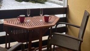 A wooden table with two red mugs and two wine glasses, positioned by a window overlooking a snowy landscape with a tall evergreen tree. - FeWo Jagsch - HarzPur - incl. bed linen and towels (Braunlage)