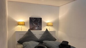 A modern bedroom with a bed, two wall-mounted lamps, and a deer painting on the wall. - FeWo Jagsch - HarzPur - incl. bed linen and towels (Braunlage)