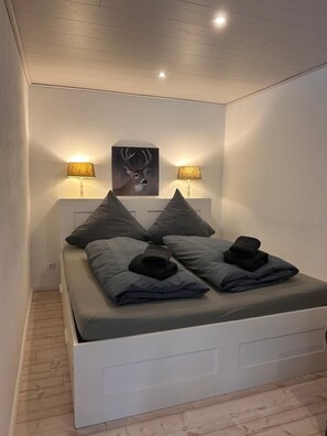 A modern bedroom with a bed, two wall-mounted lamps, and a deer painting on the wall. - FeWo Jagsch - HarzPur - incl. bed linen and towels (Braunlage)