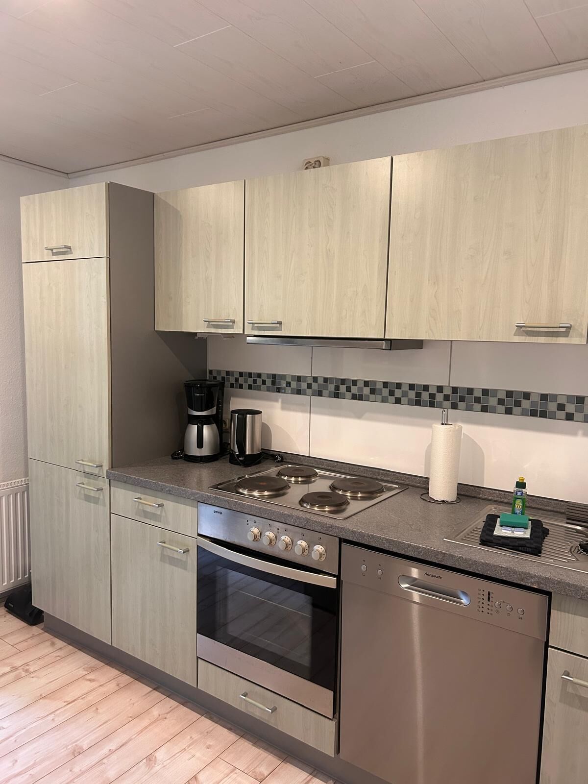 A modern kitchen with light wood cabinets, a stainless steel stove, and a dishwasher.