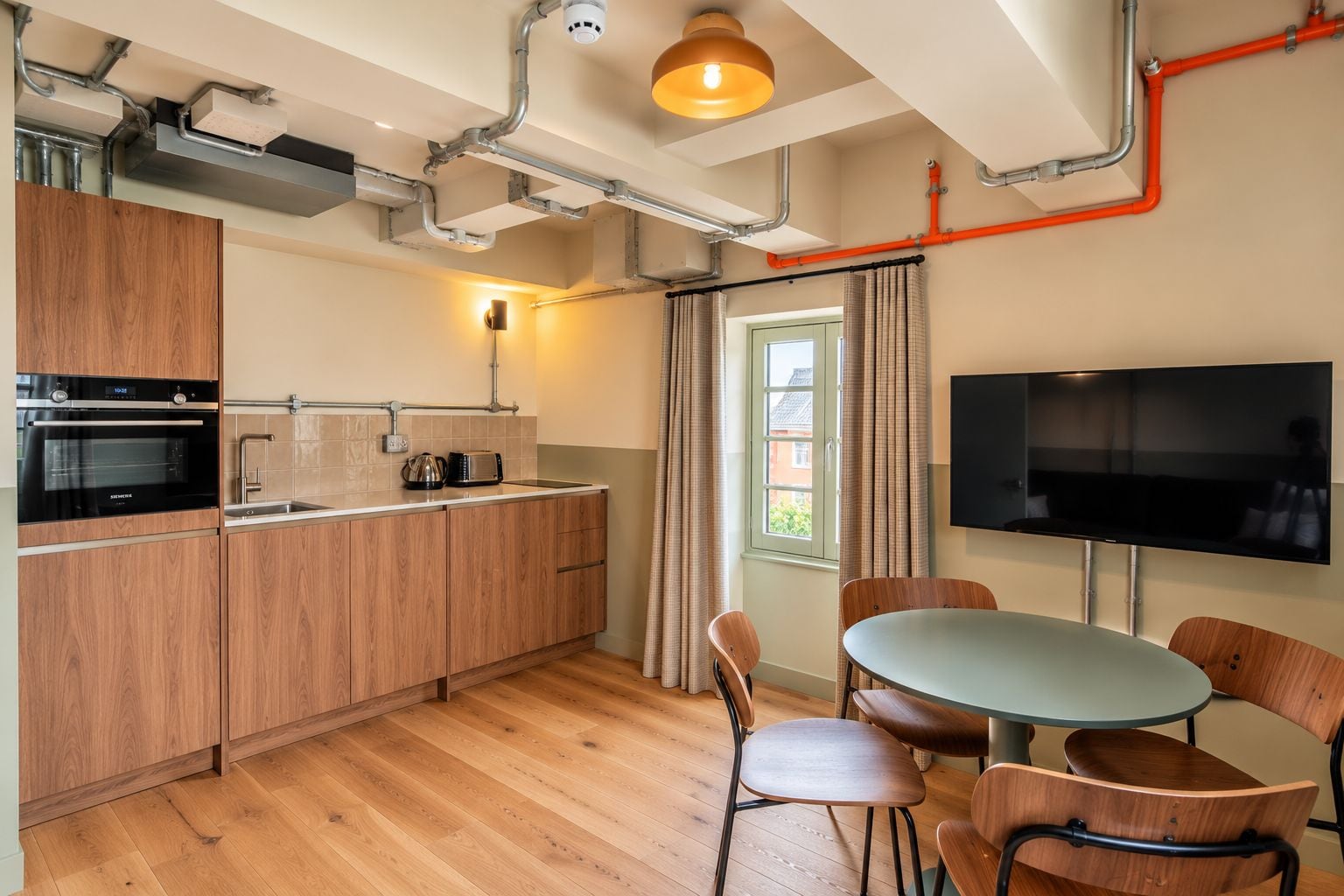 A modern kitchen with wooden cabinets, a built-in oven, and a dining area with a round table and chairs.
