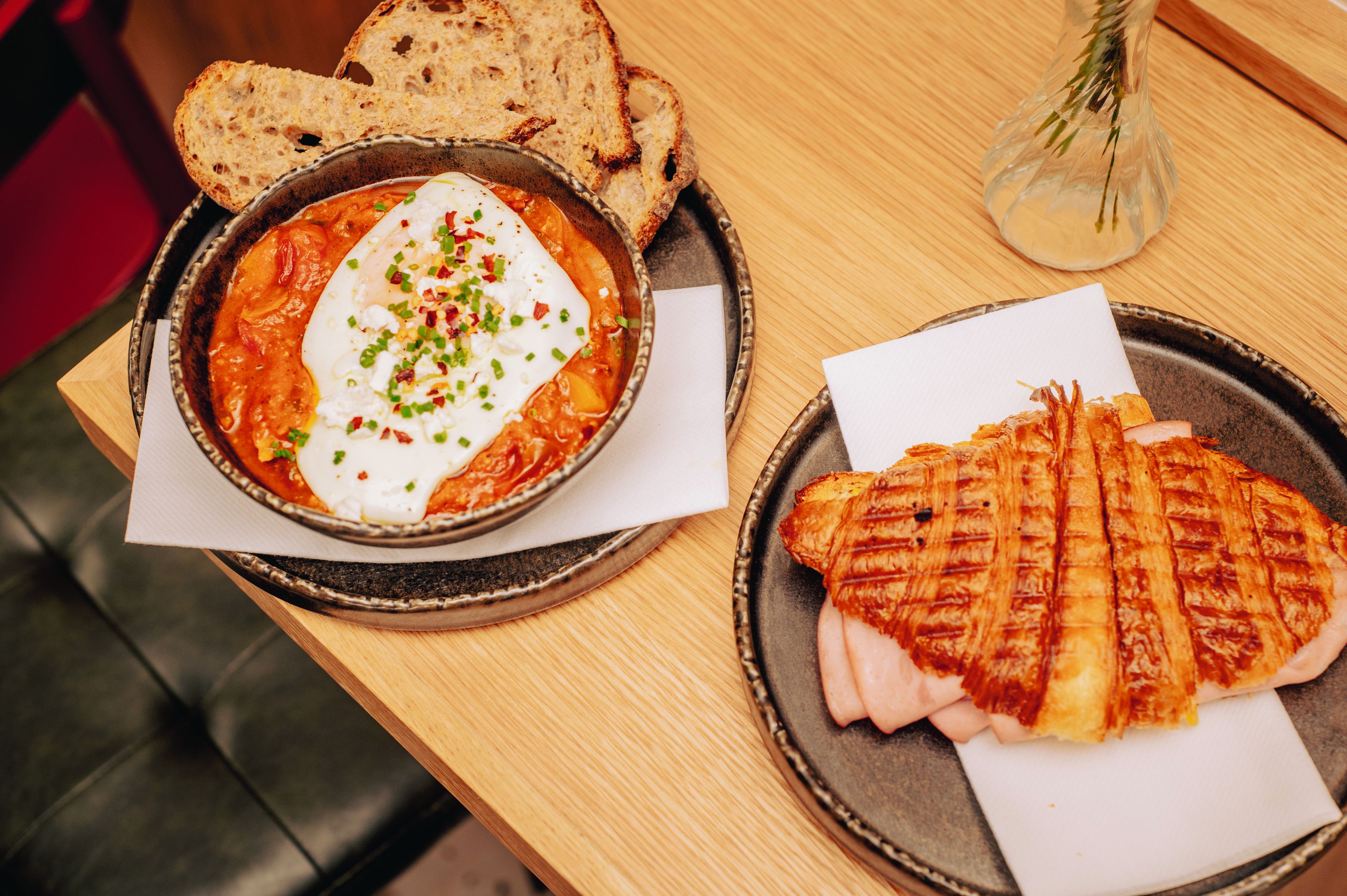 A meal consisting of a bowl of soup with a poached egg, a grilled sandwich, and slices of bread on a wooden table.