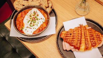 A meal consisting of a bowl of soup with a poached egg, a grilled sandwich, and slices of bread on a wooden table.
