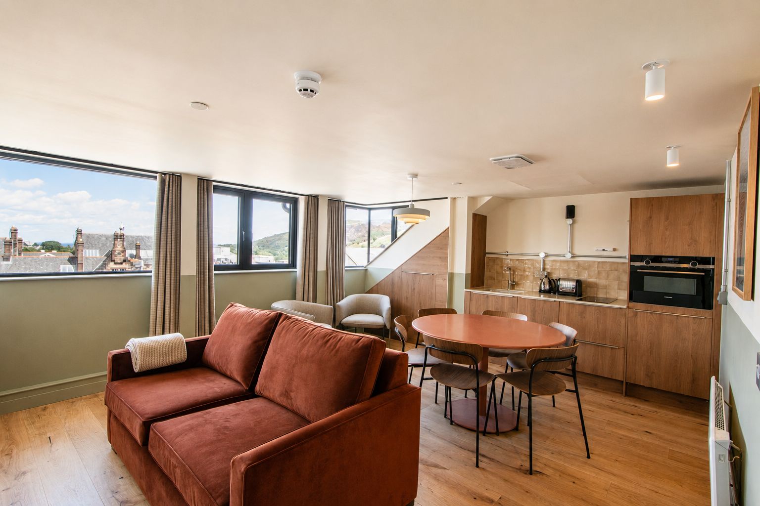 A modern interior with a sofa, dining table, chairs, kitchen area, and large windows offering a view.