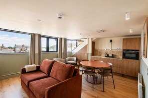 A modern interior with a sofa, dining table, chairs, kitchen area, and large windows offering a view.