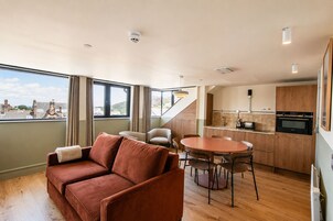 Ein modernes Interieur mit einer Couch, einem Esstisch, Stühlen, einer Küchenzeile und großen Fenstern mit Blick.
