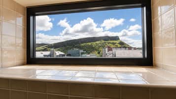 A bathroom with a large window overlooking a cityscape and a hill.