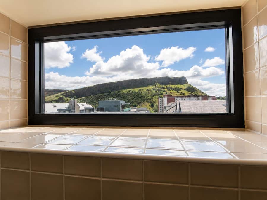 Een badkamer met een groot raam met uitzicht op een stadslandschap en een heuvel.