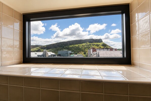 A bathroom with a large window overlooking a cityscape and a hill.