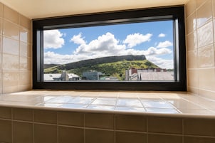 Une salle de bain dotée d’une grande fenêtre donnant sur un paysage urbain et une colline.