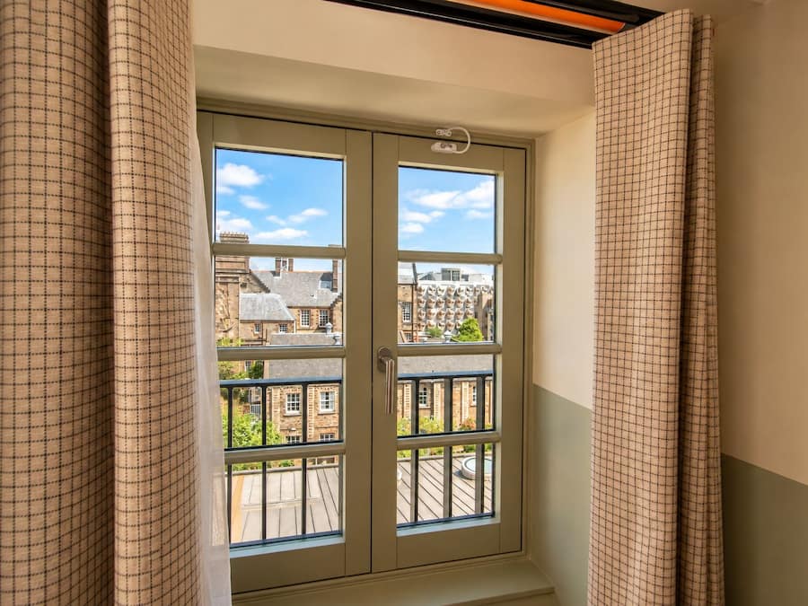 A room with a window overlooking a balcony and a cityscape.