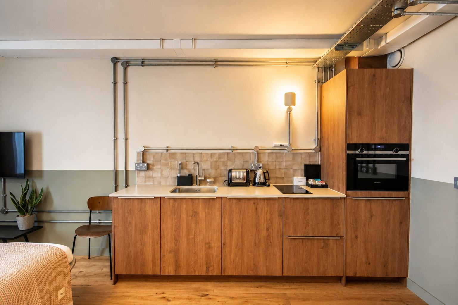 Een moderne keuken met houten kastjes, een ingebouwde oven, een koffiezetapparaat en een wandlamp.