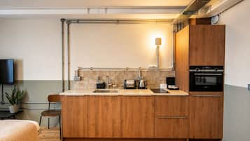 Een moderne keuken met houten kastjes, een ingebouwde oven, een koffiezetapparaat en een wandlamp.