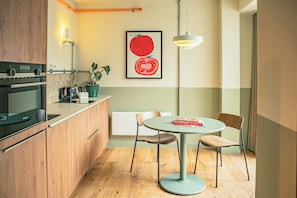 Eine moderne Küche mit Holdelementen, einem eingebauten Backofen, einem Esstisch mit Stühlen, einem Topf mit Pflanze und einem gerahmten Kunstwerk an der Wand.