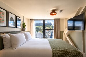 A hotel room with a large bed, a television, a window with a view of a mountain, and framed pictures on the wall.