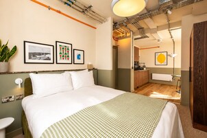 Une chambre d’hôtel avec un lit, une petite table, une plante en pot et des œuvres d’art accrochées au mur.